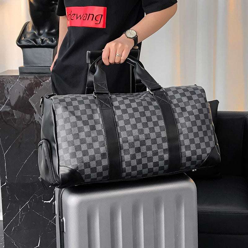Feldacks weekend bag with shoe compartment in black and gray checkered pattern being held over silver suitcase