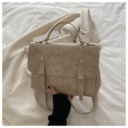 Feldacks MetroSling convertible satchel purse in beige with buckles held over a neutral fabric background
